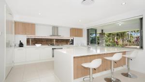 a kitchen with white cabinets and white stools at The Palms - Lennox Head in Lennox Head