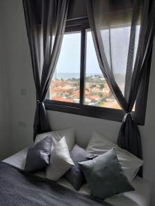 een bed met kussens in een kamer met een raam bij SEA& SUN in H̱adera