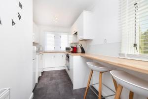 una cocina con armarios blancos y una barra con taburetes en JOIVY Bright 3-bed flat overlooking The Clyde, en Glasgow