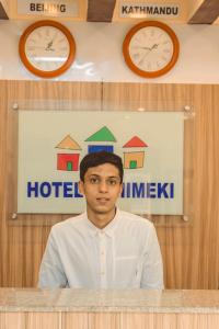 Un uomo dietro un bancone con gli orologi dietro di lui di Hotel Chhimeki a Kathmandu