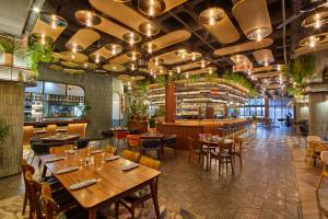 un restaurante con mesas y sillas de madera y un bar en voco Johannesburg Rosebank an IHG Hotel, en Johannesburgo