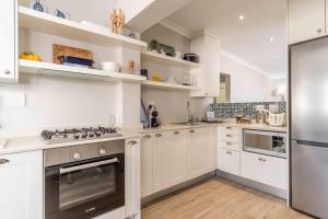 eine Küche mit weißen Schränken und einem Edelstahlkühlschrank in der Unterkunft C'estÇa Cottage Modern Luxurious Sounds of the Sea in Hermanus