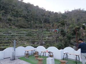 a man standing in front of a white fence with tables at Hobbit House Hostel in Rishīkesh