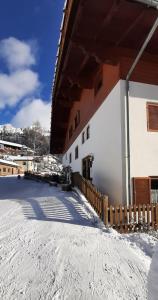 ein Gebäude mit Schnee auf dem Boden neben einem Zaun in der Unterkunft Lärchenheim in Obereggen