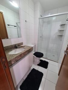 uma casa de banho branca com um lavatório e um chuveiro em Apt encantador: piscina, academia, tela proteção em Taguatinga