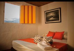a bedroom with a bed with red and orange pillows and a window at Abuela Casa Hostal in Apía