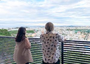 duas pessoas de pé numa varanda com vista para uma cidade em D-and Stay 5 Resort Okinawa em Urazoe
