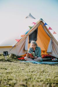 Kobieta siedząca przed namiotem czytająca książkę w obiekcie Glamping at Hay Festival w mieście Hay-on-Wye