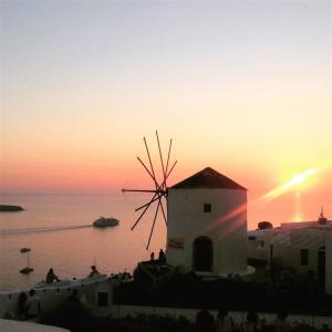 un moulin à vent en face de l'océan au coucher du soleil dans l'établissement Lioyerma Windmill Villa With Outdoor Hot Tub, à Oia