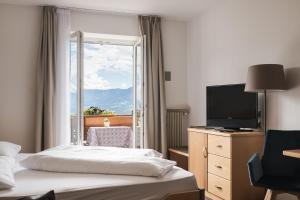 a hotel room with a bed and a tv and a window at Hotel & Residence Rebhof in Tirolo