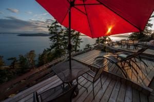 a table and chairs on a deck with a red umbrella at Shangri-La Oceanfront vacation home in Pender Island