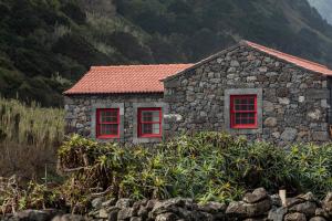 a stone house with red windows on a mountain at Kuanza Nature Experience, Fajã do Belo in Fajã da Caldeira de Santo Cristo