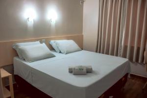a white bed with two pillows and a box on it at Palotina Palace Hotel in Palotina
