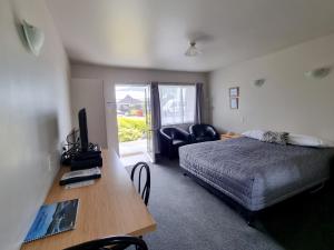 Schlafzimmer mit einem Bett und einem Schreibtisch mit einem TV in der Unterkunft ASURE Gables Motor Lodge in Greymouth