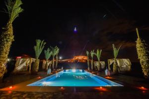 a swimming pool at night with palm trees at Agafay Pearl Camp Marrakech in Marrakech