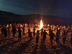 un gruppo di persone che ballano intorno al fuoco sulla spiaggia di Ming Sha Mountain Wild Hostel a Dunhuang