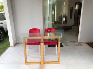 um gato sentado numa mesa de vidro com duas cadeiras vermelhas em Casa duplex de temporada em Imbassai em Imbassaí