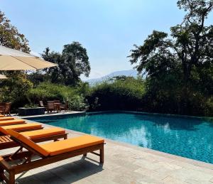 a swimming pool with lounge chairs and an umbrella at The Postcard Hideaway, Netravali Wildlife Sanctuary, Goa in Vichondrem