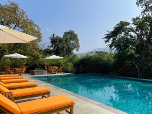 The Postcard Hideaway, Netravali Wildlife Sanctuary, Goa في Vichondrem: مسبح بكراسي برتقال ومظلات