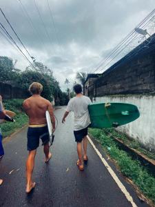 Dois homens a descer uma estrada com uma prancha de surf. em Nature Rex Hostel em Weligama