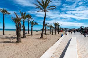 a beach with palm trees and people walking on it at Brand new Javea apartment 50m from Arenal beach in Jávea