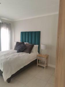 a bedroom with a bed with a green headboard and a table at The Blyde apartment NO BRAAI OR PARTY in Pretoria