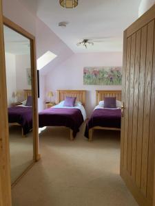 1 Schlafzimmer mit 2 Betten mit lila Bettwäsche und einem Spiegel in der Unterkunft Tulach Ard in Grantown on Spey