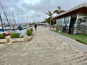 a man walking down a sidewalk next to a marina at Barco TUAREG in Puerto Calero