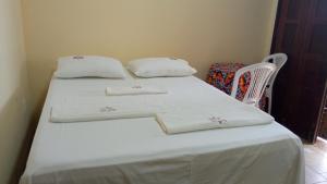 uma cama com duas almofadas e uma cadeira num quarto em POUSADA CANEDO em Guaibim