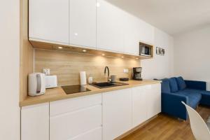 a kitchen with white cabinets and a blue couch at Apartament Piaskowy Sunset Resort in Grzybowo