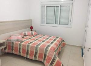 a bedroom with a bed with a plaid blanket and a window at Residencial Lazzari Apto 402 in Arroio do Sal