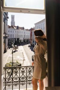 a woman standing in front of a window looking out at Hotel du Théâtre in Bruges