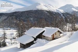 a house covered in snow with a mountain in the background at Baita Hanzel e Gretel in Livigno