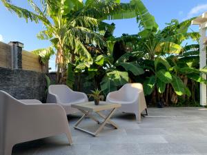 a patio with white chairs and a table and trees at Chez BIBI in Grand-Bourg