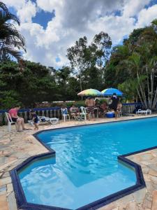 a swimming pool with people sitting in chairs and umbrellas at Hospedagem Chalé pousada Chácara Cantinho do Mozão in São Roque