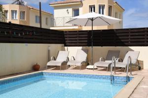 a pool with chairs and an umbrella next to a house at Pedalion Villa in Protaras