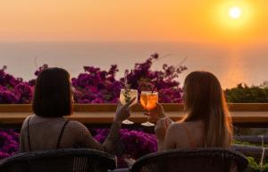 two women sitting in chairs holding drinks in front of the sunset at Hotel Il Girasole in Anacapri