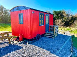 a red tiny house sitting on gravel next to a picnic table at Shepherds Hut Glamping in Bantry