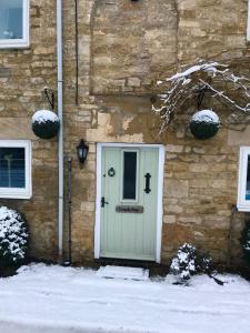 a stone house with a green door in the snow at Turnpike Cottage in Tetbury