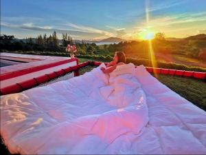 a person laying on a bed in front of the sunset at บ้านฟาร์มรักพูลวิลล่าวิวทะเลสาปแก่งกระจาน in Ban Khao Dok Mai