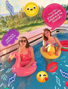 dos chicas sentadas en el agua en una piscina en บ้านฟาร์มรักพูลวิลล่าวิวทะเลสาปแก่งกระจาน en Ban Khao Dok Mai