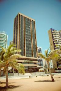 a tall building with palm trees and palm trees at Carmel Magna Praia Hotel in Fortaleza