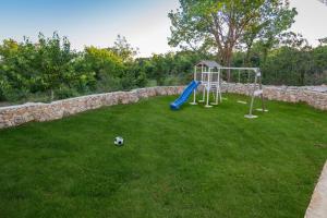 a playground in a yard next to a stone wall at Luxury Villa Paloma Blanca with Heated Pool in Lovreć