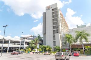 un grand bâtiment avec des voitures garées dans un parking dans l'établissement Hotel Trinitarias Suites, à Barquisimito