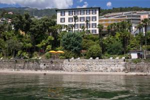 uma praia com um guarda-sol e alguns edifícios e água em Hotel Garni Rivabella au Lac em Brissago