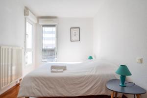 a white bedroom with a bed and a table with a lamp at Le Zénith - GOLDEN TREE - Parking privé & WIFI - 5 min Zénith de Strasbourg in Strasbourg