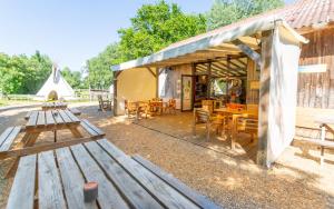 a patio with wooden tables and chairs and a building at Les Tipis du Bonheur de Vivre in Brûlon