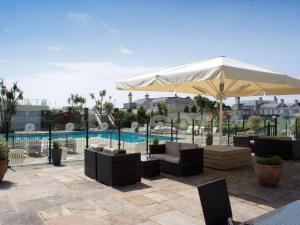 un patio con una sombrilla y sillas blancas y una piscina en TLH Victoria Hotel - TLH Leisure, Entertainment and Spa Resort, en Torquay