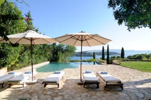 a group of chairs and umbrellas next to a pool at Beachfront Villa in Porto Heli
