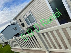 ein Haus mit einem Zaun mit grünen Buchstaben darauf in der Unterkunft Summer Breeze Deluxe Caravan Rental in Saint Osyth